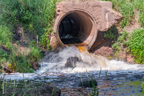 A view of the stormy flow of clear water from the culvert on a bright summer sunny day