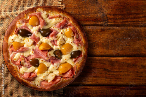 Sweet pizza with peaches, fig and pineapple on wood background. Top view, close up. Traditional Brazilian Pizza