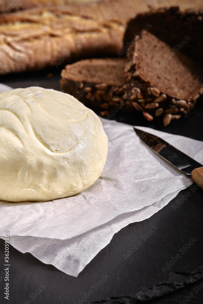 Loaf of bread with butter and knife. Dark background, side view Loaf of bread with butter and knife. Dark background, side view