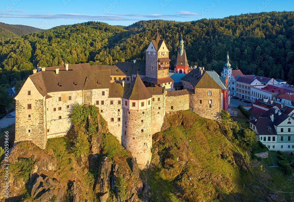 Aerial view of Loket Castle, Burg Elbogen, gothic style castle on rocky cliff, surrounded by green hills. Massive fortification illuminated by setting sun. Karlovy Vary district, Czechia Aerial view of Loket Castle, Burg Elbogen, gothic style castle on rocky cliff, surrounded by green hills. Massive fortification illuminated by setting sun. Karlovy Vary district, Czechia