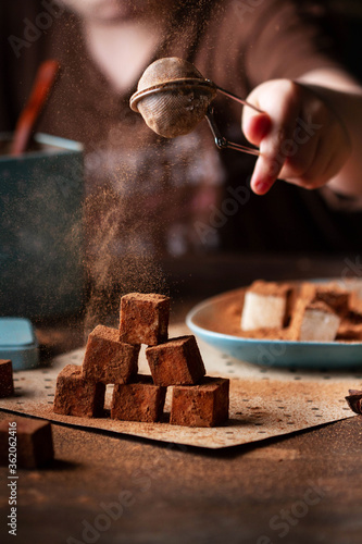 A hand sprinkles cocoa from a strainer onto a bird's milk turret.