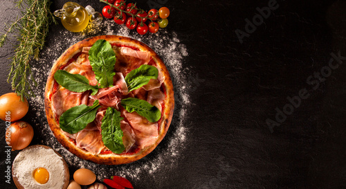 Brazilian pizza with prosciutto and arugula. Top view on black concrete background, close up. Traditional Brazilian Pizza