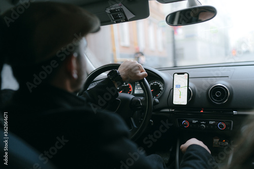 Male taxi driver in beret rides behind the wheel of car and looks at navigator