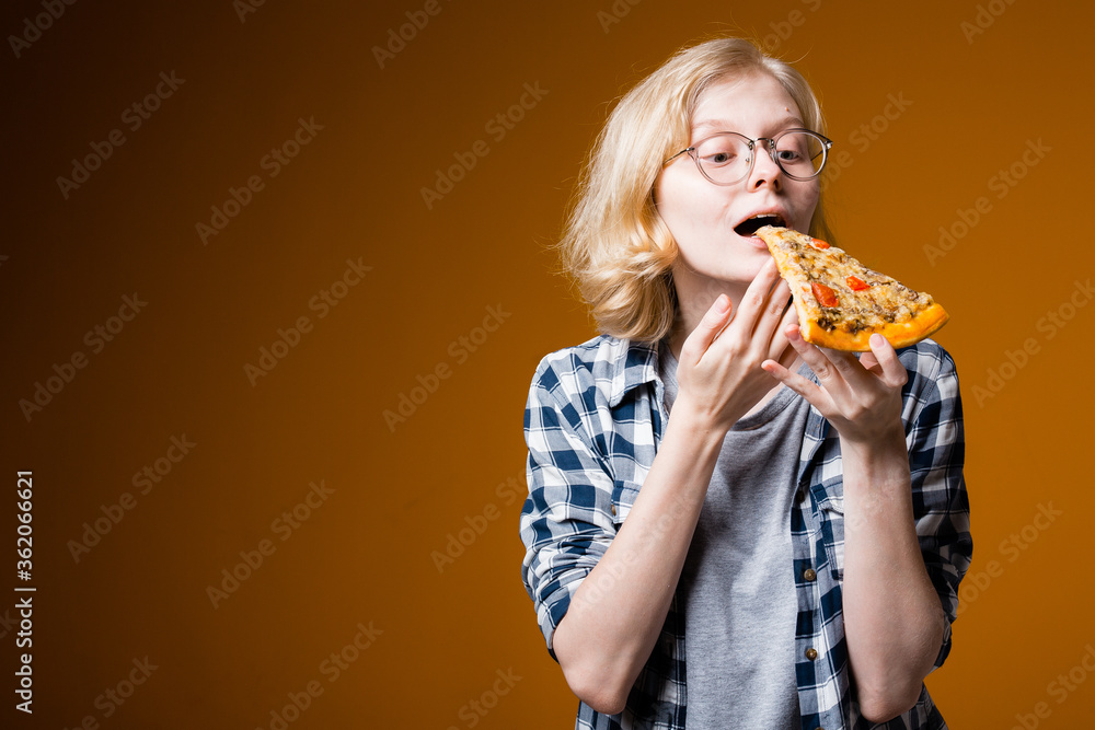 A Swedish girl with glasses brings a piece of pizza to her mouth in preparation for a bite. Advertising banner for pizzeria on an orange background