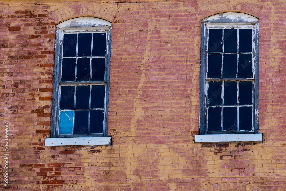 Two old windows with peeling paint set in an old red brick wall