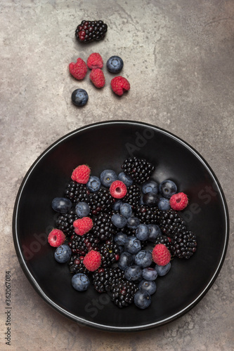 Berries in black ceramic plate: blackberry, cherry, blueberry and raspberry. Gray background.