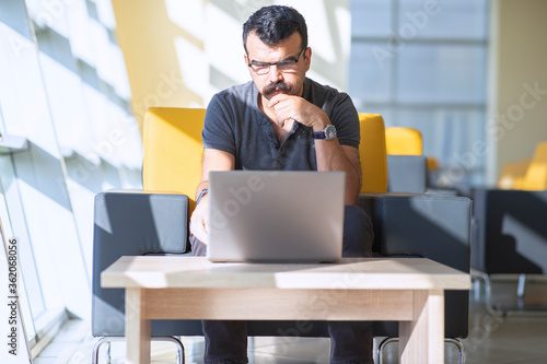 Photos Concentrated toughtful man is looking to laptop screen  in a modern office