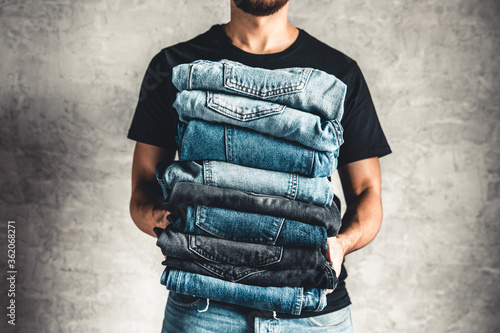 close up stack of folded denim blue jeans in hand over gray wall background, copy space