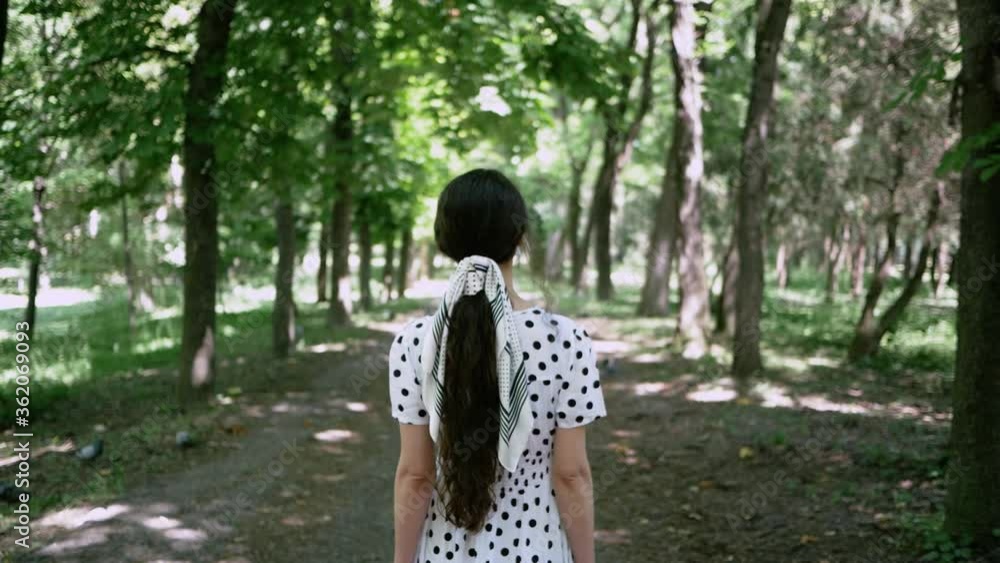 Young woman in white dress goes in Park in summer, view from back. She turns to face camera on her protective mask from an Allergy or virus