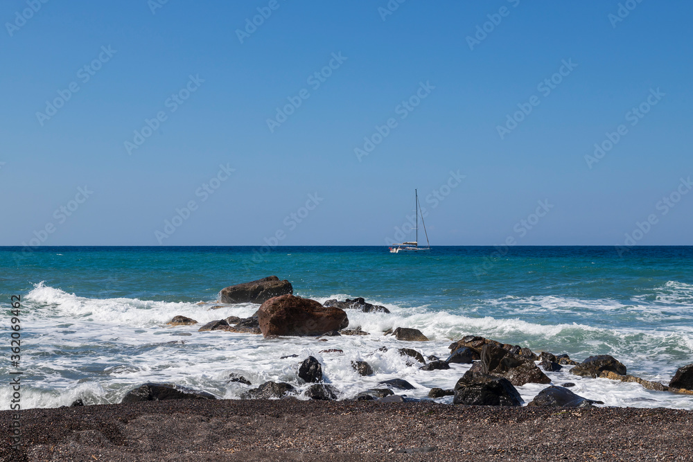 Coast and beach of Vlychada on Santorini island in Greece. In the background blue sky and waves at sea.