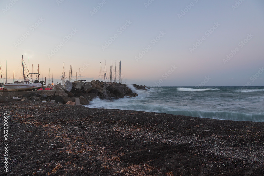 Boats in Vlichada harbor on Santorini island in Greece in the morning at sunrise. The background is a blue sky with white clouds and rising sun. Boats in Vlichada harbor on Santorini island in Greece in the morning at sunrise. The background is a blue sky with white clouds and rising sun.