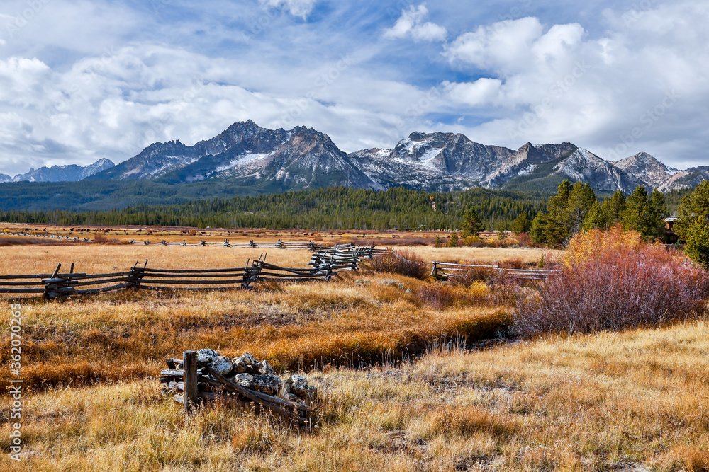 A split rail fence on the border of a large meadow with the Sawtooth mountains in the background, in the fall season near Stanley, Idaho.