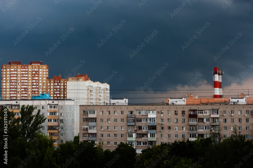The sky is very dark blue over multi-storey buildings before a thunderstorm, with pipes visible on the horizon The sky is very dark blue over multi-storey buildings before a thunderstorm, with pipes visible on the horizon