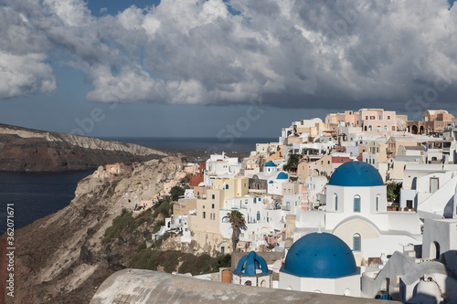 Oia town on Santorini island in Greece. The background is a blue sky with dark clouds. View of white houses