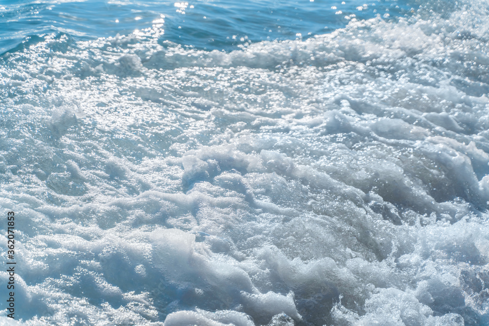 Texture Light blue surface of raging sea water with white foam and wave pattern.The azure surface of the ocean. Waves break at the shore. Azure sea of bubbling foam natural background.