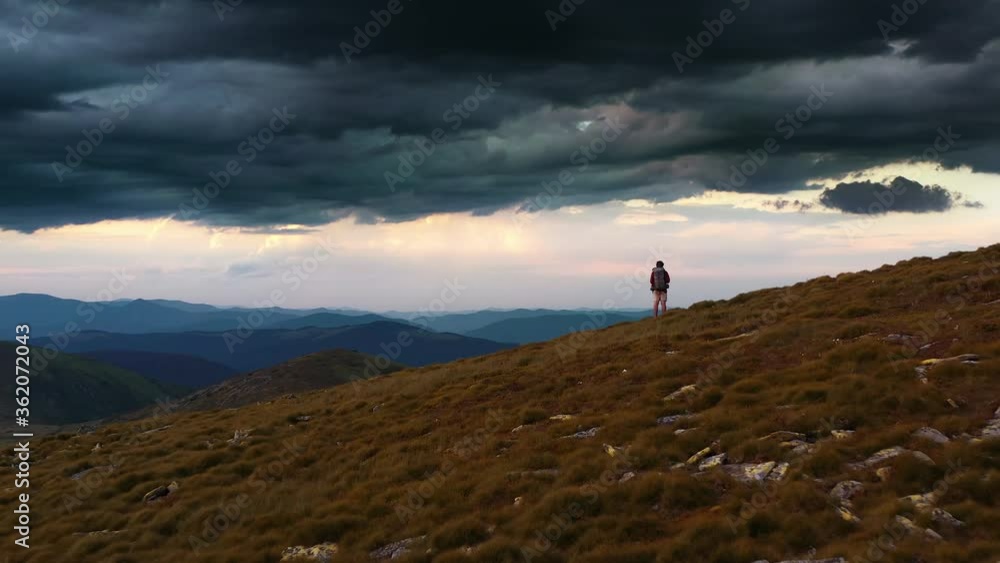 Man standing on rock with epic mountain viewpoint with a colorful sunset drone aerial landscape shot. Sun rays emerging though the dark storm clouds in the mountains Man standing on rock with epic mountain viewpoint with a colorful sunset drone aerial landscape shot. Sun rays emerging though the dark storm clouds in the mountains