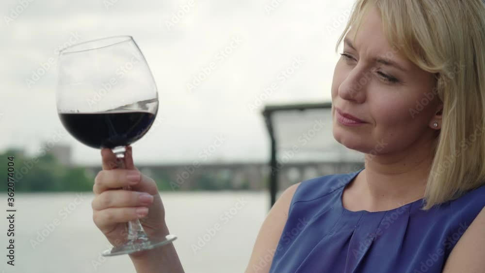 Close-up of smiling blond woman enjoying red wine outdoors. Side view portrait of elegant Caucasian lady drinking beverage in outdoor waterfront restaurant. Leisure, resting, lifestyle, joy. Close-up of smiling blond woman enjoying red wine outdoors. Side view portrait of elegant Caucasian lady drinking beverage in outdoor waterfront restaurant. Leisure, resting, lifestyle, joy.
