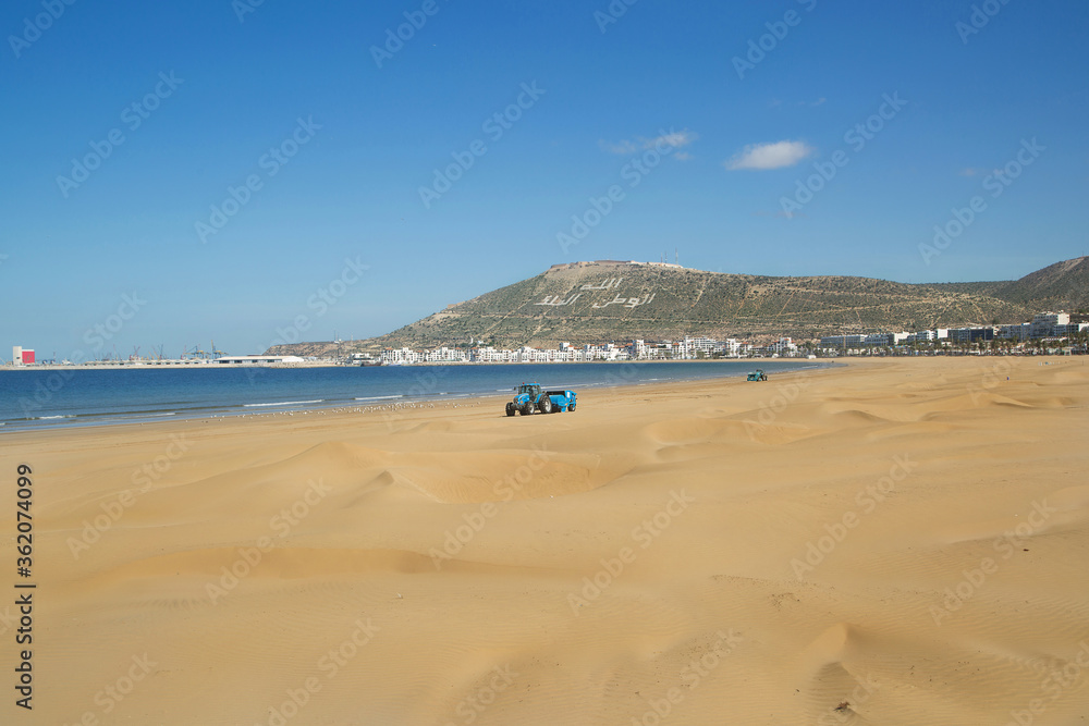 beach of Agadir Morocco, name of the mountain Oufellah, inscription: God, country, king. tractor levels the sand on the beach