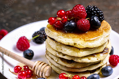 Sweet Homemade Pancakes with berries, honey or maple syrup on black background. Morning breakfast concept.