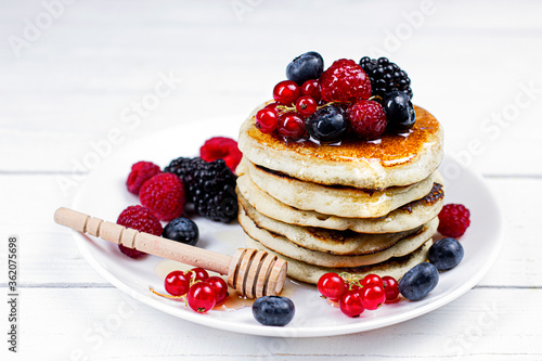 Sweet Homemade Pancakes with berries, honey or maple syrup on white background. Morning breakfast concept.