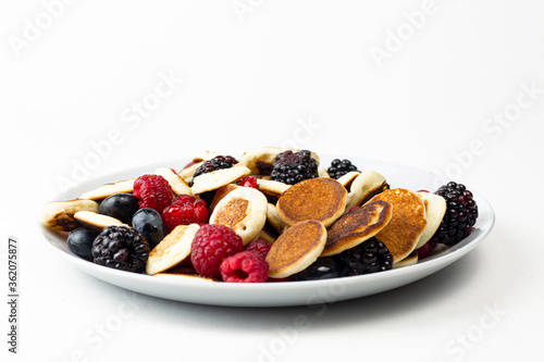 Trendy mini pancakes breakfast concept. Tiny cereal Pancakes with berries, honey or maple syrup on white background. Kids lovely breakfast concept.