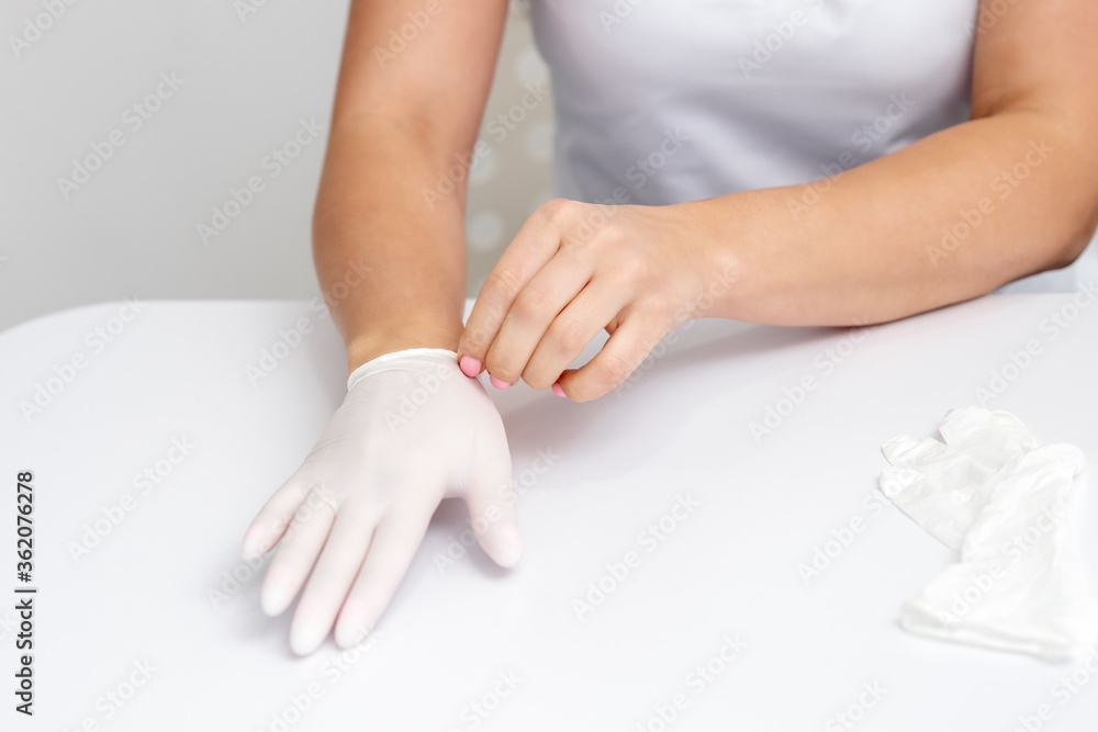 Obraz premium Female hands putting on protective white latex medical gloves during epidemic in quarantine