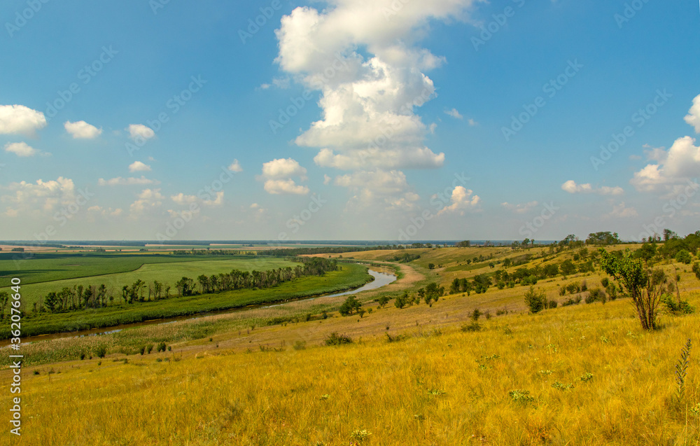 Beautiful view from the hill on the blue sky, the river and agricultural fields extending beyond the horizon.