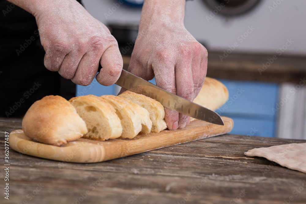 Striped baguette on a board. The knife is in men's hands. Kitchen view
Striped baguette on a board. The knife is in men's hands. Kitchen view