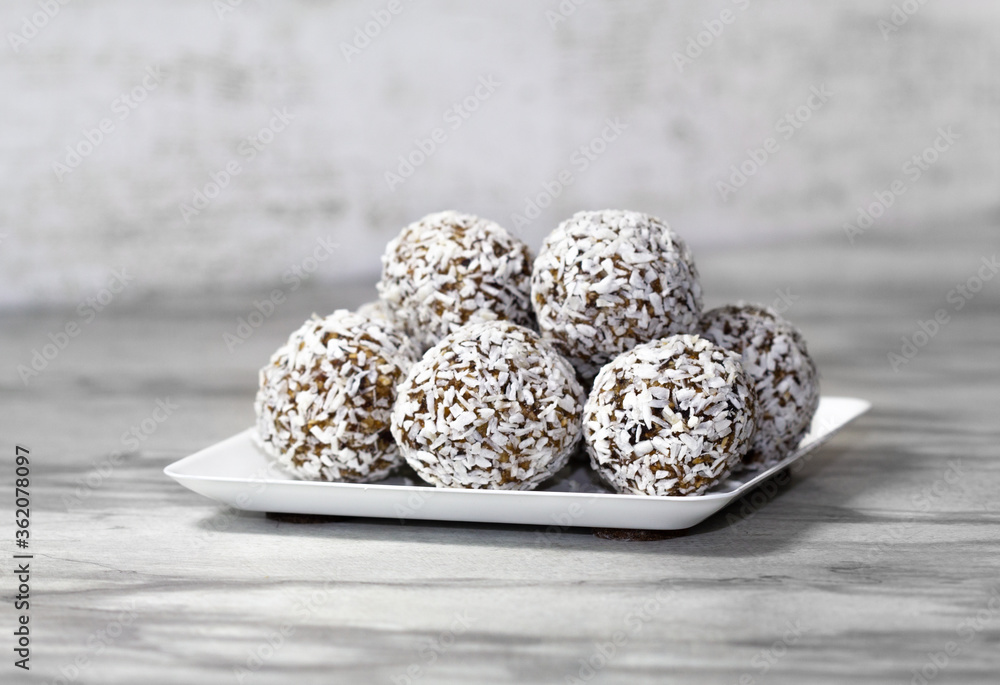Homemade energy balls with dried apricots, raisins, dates, prunes, walnuts and coconut. Healthy sweet food. Energy balls in a plate on a marble gray background. Close up. Side view. Copy space