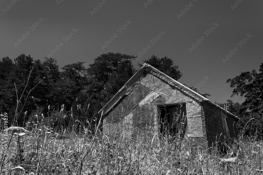 desolated scene of a metal house abandoned in the middle of a field wit a forest behind it desolated scene of a metal house abandoned in the middle of a field wit a forest behind it