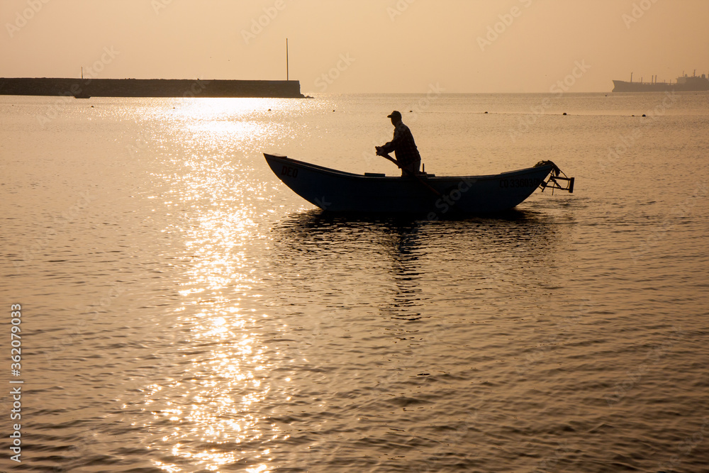 silhouette of man rowing fishing boat in water during dusk and golden hour in Lima Peru