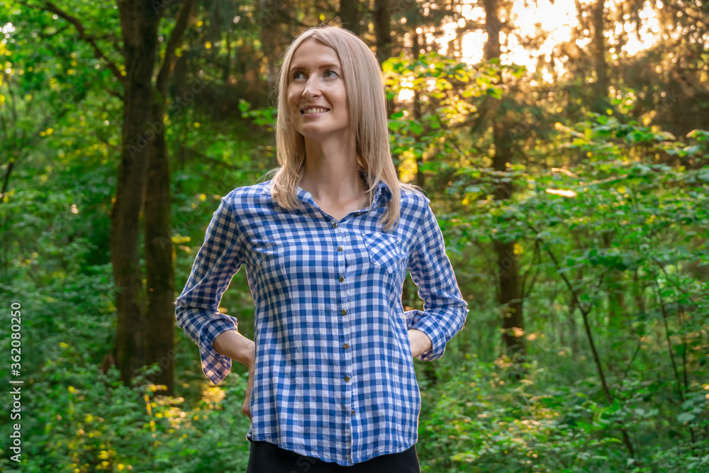Portrait of a beautiful smiling European blonde girl in a shirt in the forest at sunset, copy space. Portrait of a beautiful smiling European blonde girl in a shirt in the forest at sunset, copy space.