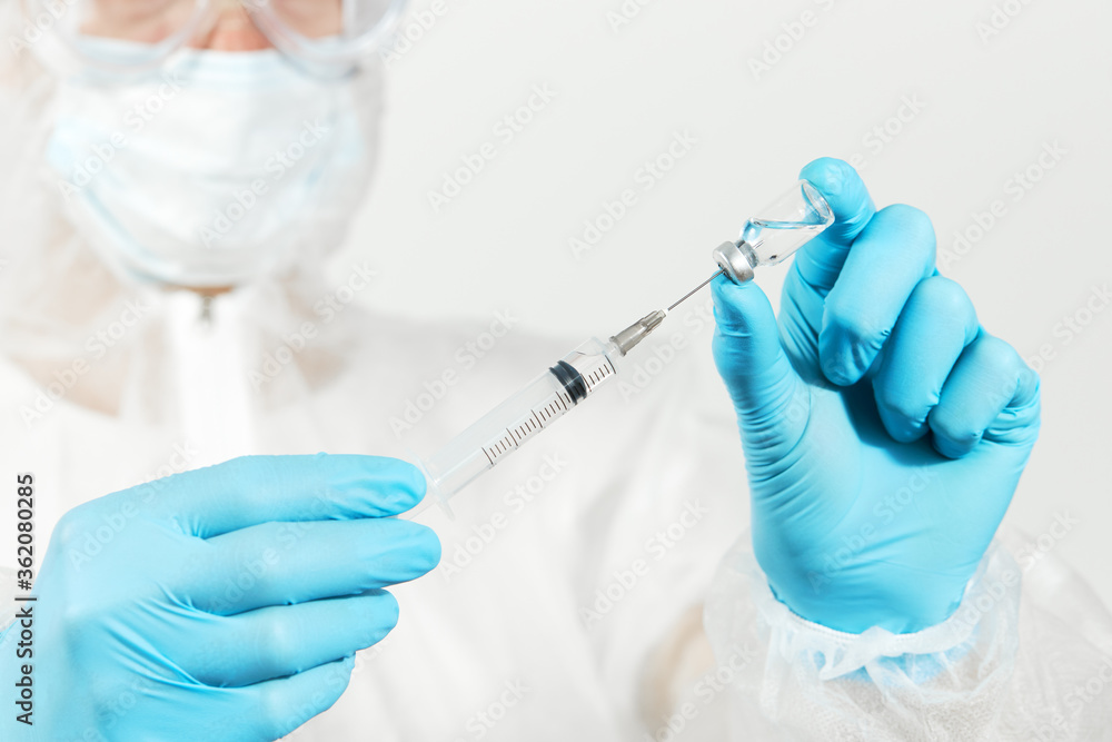 Male doctor in blue nitrile gloves, glasses and a respirator mask for protection holds a vaccine bottle and syringe for injection. Coronavirus Vaccine concept. Male doctor in blue nitrile gloves, glasses and a respirator mask for protection holds a vaccine bottle and syringe for injection. Coronavirus Vaccine concept.