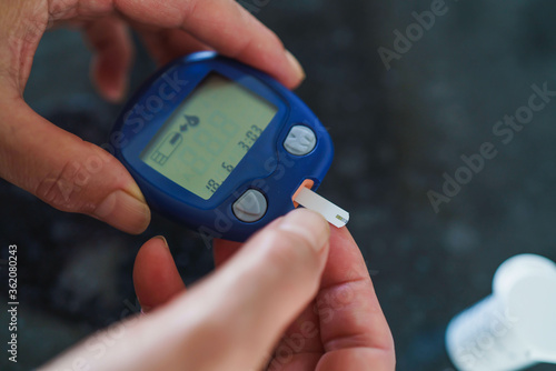Medicine, Diabetes, Glycemia, Health care and people concept - close up of female using lancelet on finger to checking blood sugar level by Glucose meter