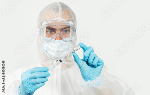 Male doctor  in blue nitrile gloves, glasses and a respirator mask for protection holds a vaccine bottle and syringe for injection. Coronavirus Vaccine concept.