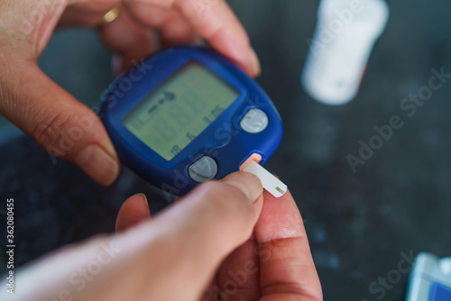 Medicine, Diabetes, Glycemia, Health care and people concept - close up of female using lancelet on finger to checking blood sugar level by Glucose meter photo