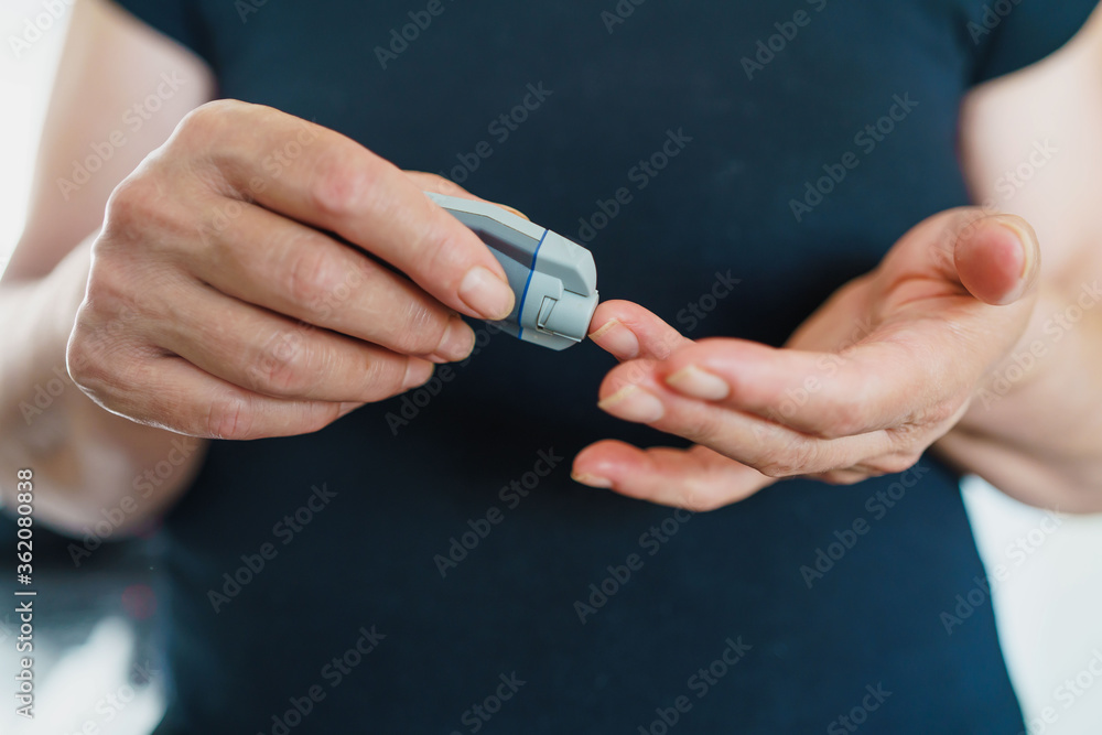 Fototapeta premium Medicine, Diabetes, Glycemia, Health care and people concept - close up of female using lancelet on finger to checking blood sugar level by Glucose meter
