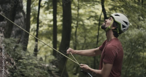 Climber with beard and helmet protect rock climb partner safety belay rope pull brake outdoors lifestyle sport in forest nature