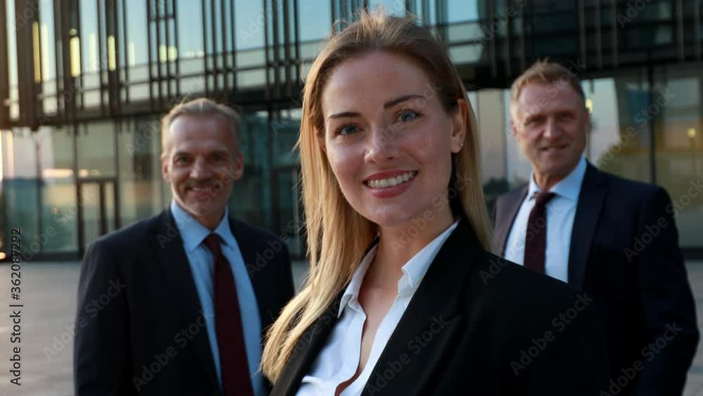 Confident business woman in front and the team in background. Business building exterior Confident business woman in front and the team in background. Business building exterior