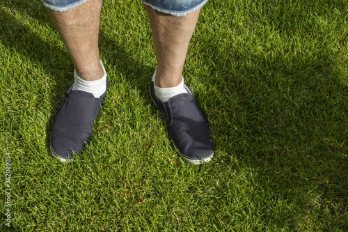 Close up view of male feet in black sneakers on green grass lawn on sunny day. Summer men shoes.