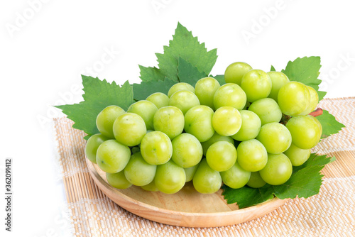 Sweet Green grape on wooden plate isolated on white. Shine Muscat Grape with leaves on white.