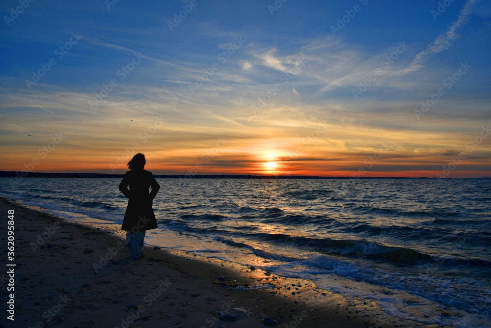 A young woman watches the beautiful and colorful sunset at the West Meadow beach,  Stony Brook, New York. 