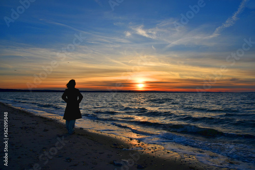 A young woman watches the beautiful and colorful sunset at the West Meadow beach, Stony Brook, New York. 