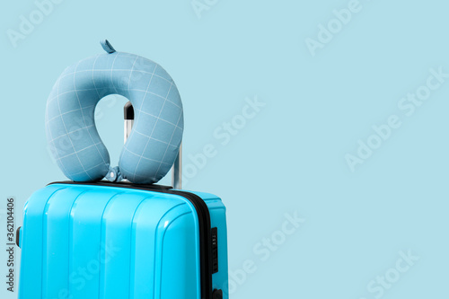 Packed suitcase and travel pillow on color background