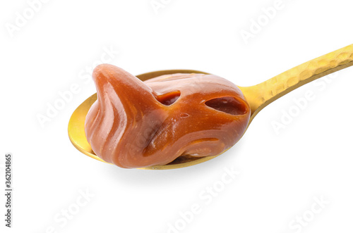 Spoon with liquid caramel on white background