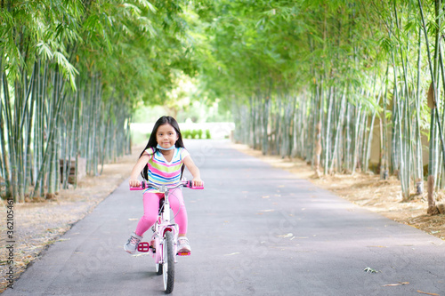 Wallpaper Mural Asian child smile or kid girl wear face mask under chin and cycling fun on bike or people bicycle on public park with green garden and bamboo tree for sport exercise to healthy on summer relax holiday Torontodigital.ca