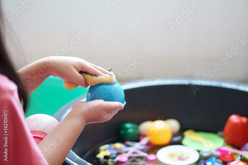 closeup hand of child or kid girl wash and cleaning colorful plastic toy in water basin black by sponge for kill bacteria or dirty disease and dust sterilize from coronavirus covid-19 photo