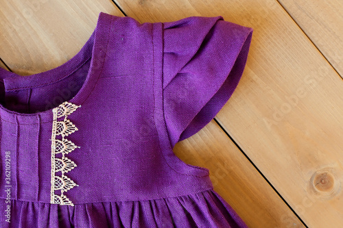 Children's dress made of bright purple linen. Element of the design of lace is sewn in close-up.