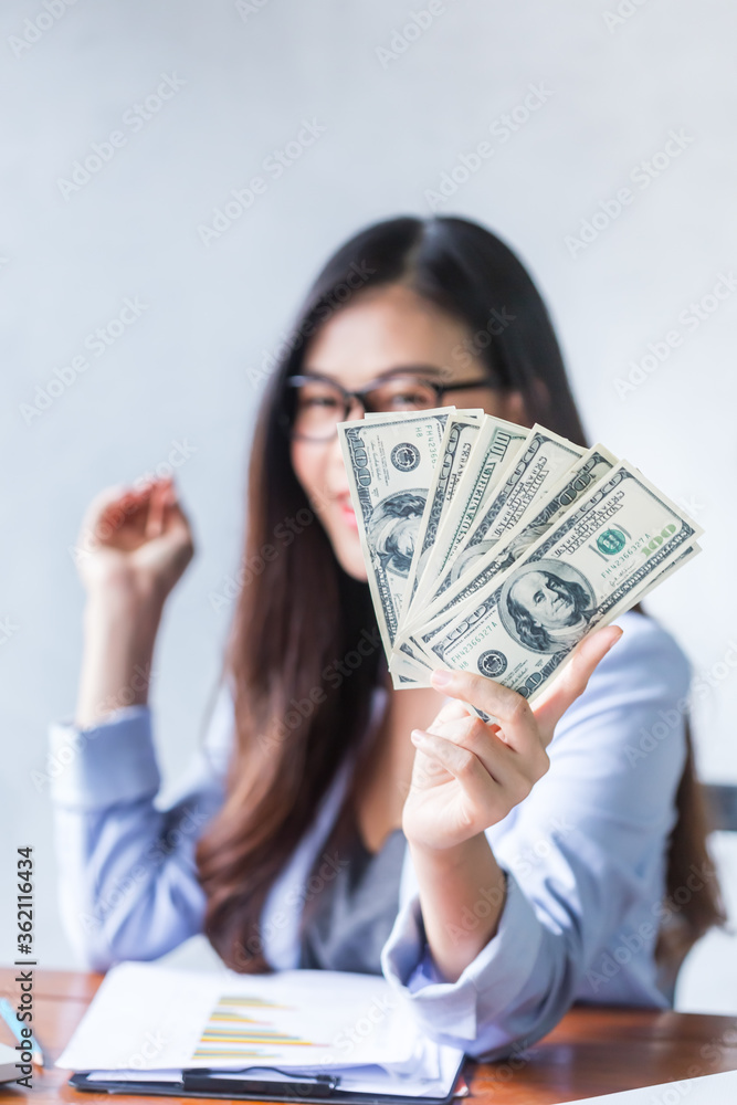 Beautiful business woman sitting at home office desk  using a laptop and smiling while working with banknote hold in hand, and and be attractive cheerful model using computer. Indoors