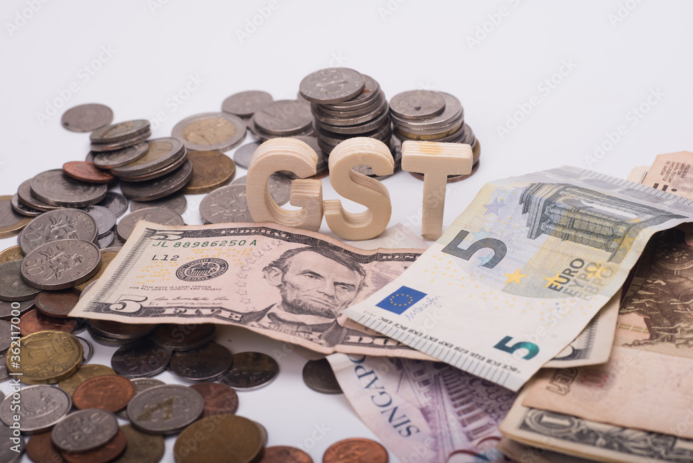 GST wooden alphabet over spread of bank notes and coins over white